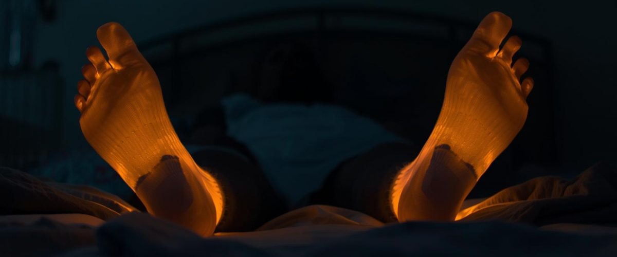 Article (16_9)_ a person wearing socks to bed or in bed at night and the socks are glowing orange