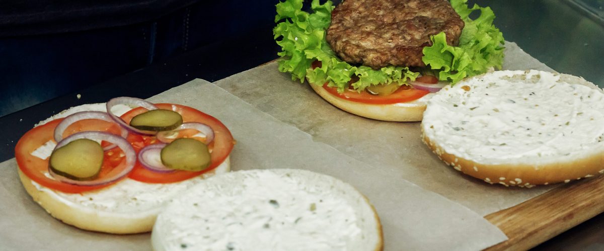 process of making burger. cooking hamburgers and cheeseburgers, putting ingridients on wooden desk. catering in food court at mall concept. space for text