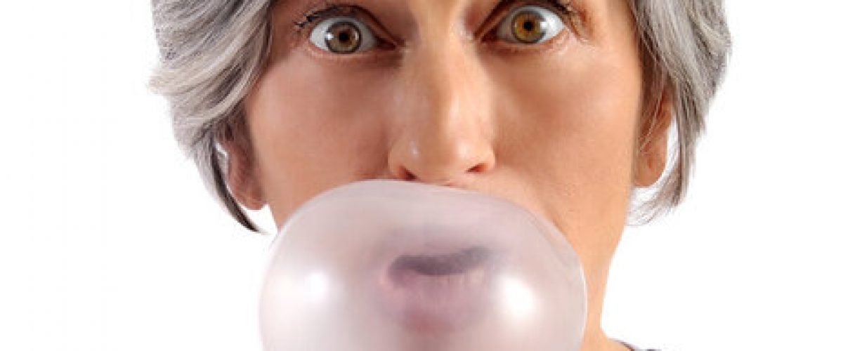 Adult Woman with Short Gray Hair Blowing Chewing Gum with Eyes Wide Open Looking at Camera. Isolated on White Background.