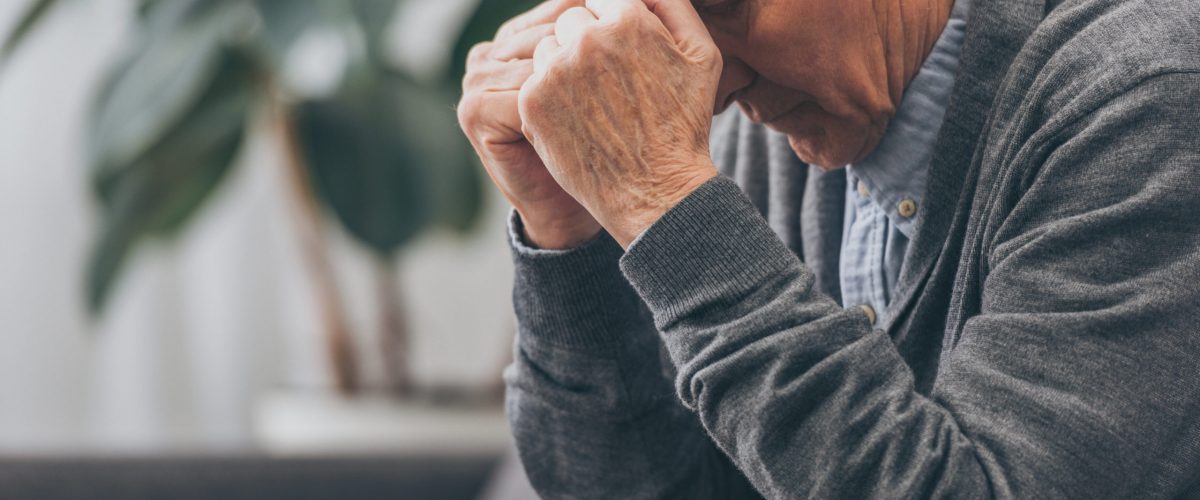 selective focus of upset retired man holding head while sitting on sofa